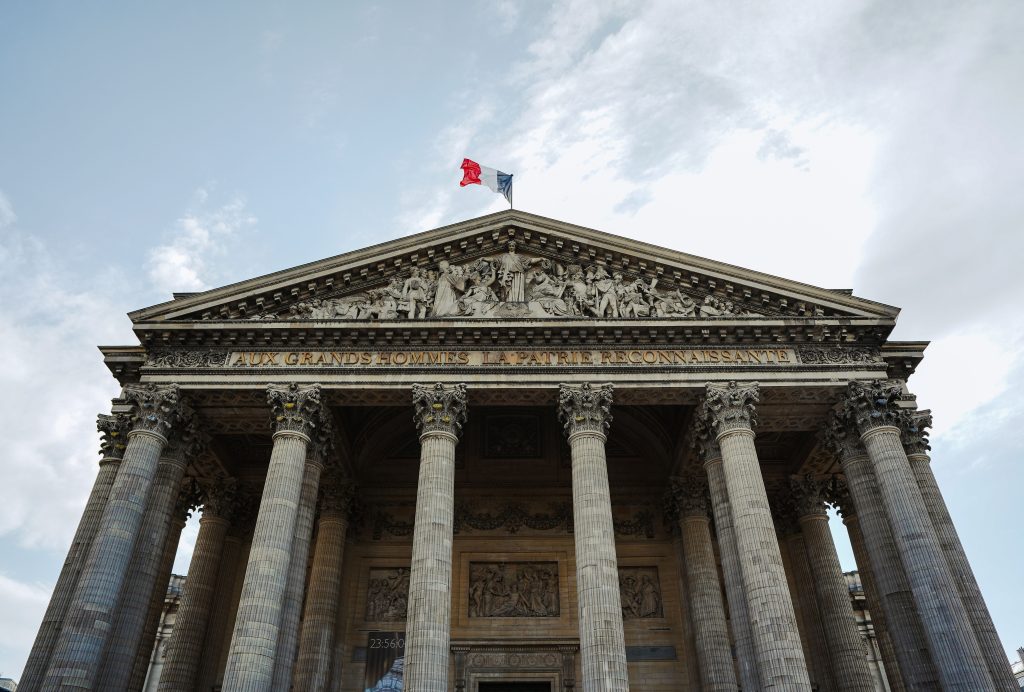 Classical architecture of the Pantheon in Paris with a French flag waving atop.