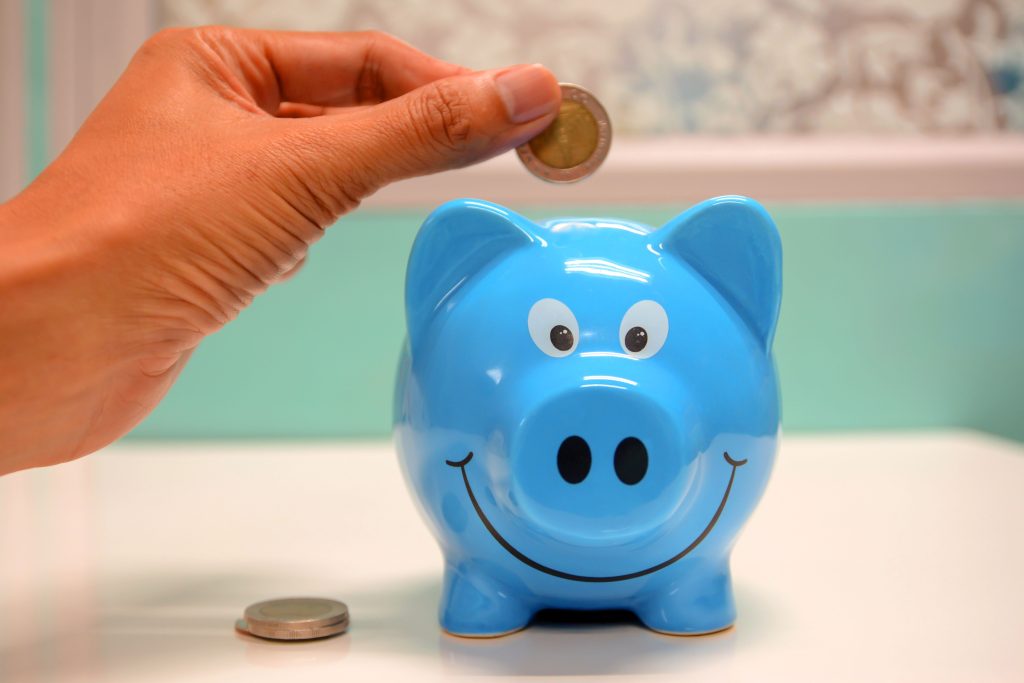 Stratégies efficaces pour économiser de l'argent et accroître sa capacité d'épargne Hand inserting a coin into a blue piggy bank for savings and money management.
