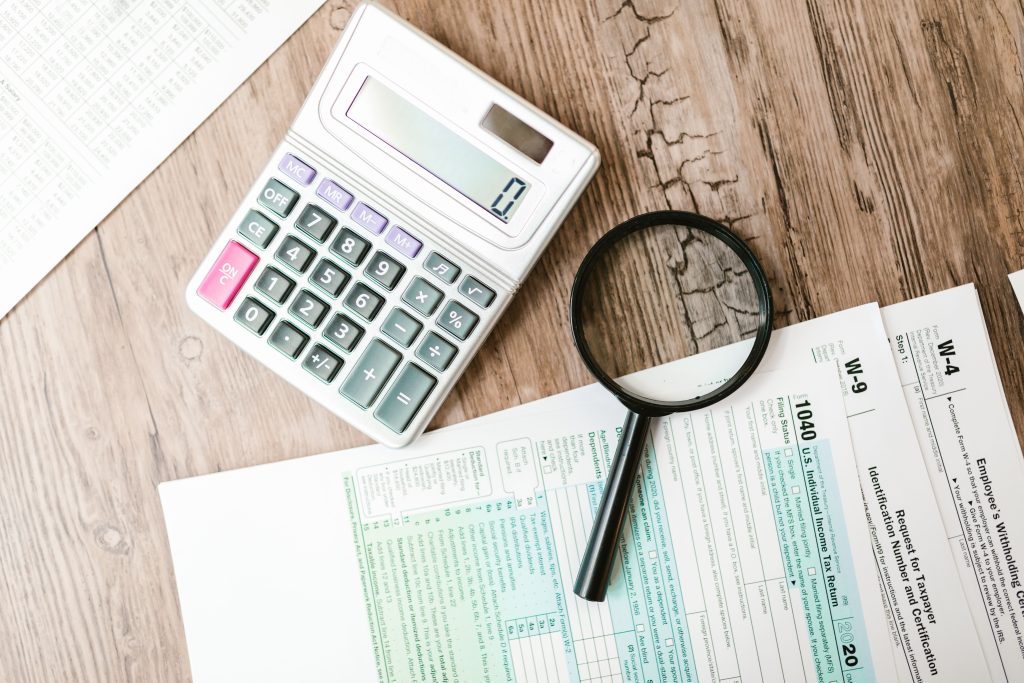 Stratégies efficaces pour économiser de l'argent et accroître sa capacité d'épargne Tax forms laid out with a calculator and magnifying glass on a wooden surface, perfect for finance themes.