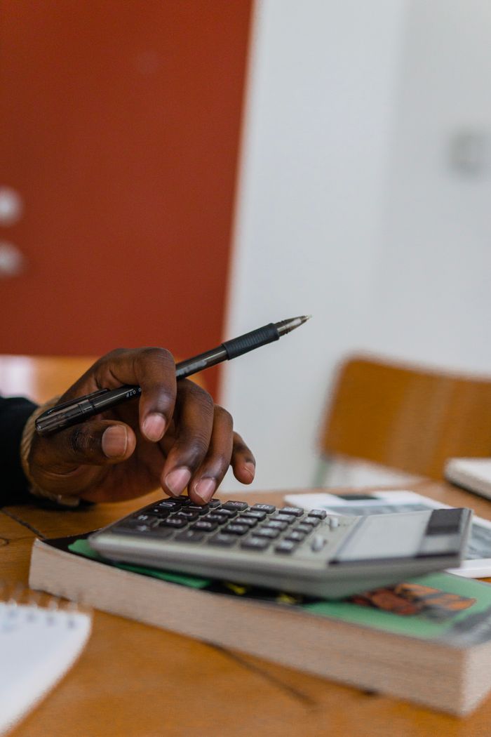 services-03 Close-up shot of a hand holding a pen while calculating finances with a calculator on a table.