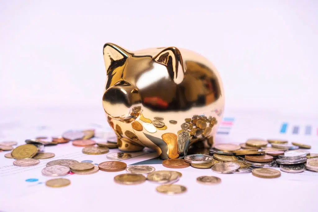 Comment épargner avec un petit budget : La méthode 50/30/20 expliquée Shiny golden piggy bank on financial documents with scattered coins symbolizes savings.